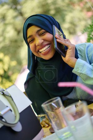 Téléchargez les photos : Une femme musulmane afro-américaine sereine en hijab engage une conversation paisible sur son téléphone portable au milieu de la beauté tranquille de la nature - en image libre de droit