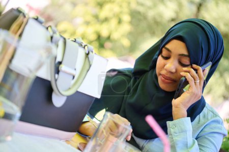 A serene African American Muslim woman in hijab engages in a peaceful conversation on her cellphone amidst the tranquil beauty of nature 