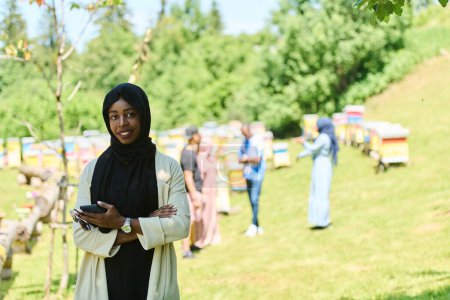 Téléchargez les photos : Femme musulmane du Moyen-Orient dans un hijab utilise un smartphone tout en gérant une petite entreprise apicole, mélangeant la technologie moderne avec les pratiques traditionnelles - en image libre de droit