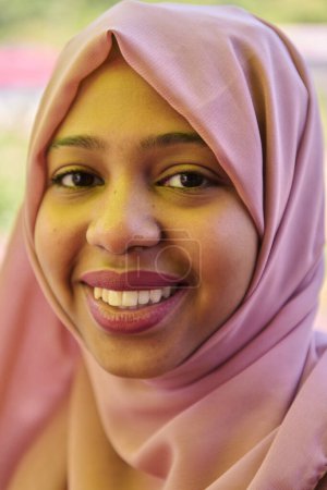 Foto de Una chica de Oriente Medio que lleva un hijab, con una sonrisa brillante y un pañuelo rosa en la cabeza, capturado en un retrato de cerca que exuda alegría y positividad. - Imagen libre de derechos