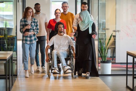 A diverse group of young business people congregates within a modern startups glass-enclosed office, featuring inclusivity with a person in a wheelchair, an African American young man, and a hijab
