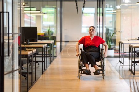 Une jeune femme d'affaires moderne en fauteuil roulant est entourée d'un espace de travail inclusif avec des bureaux vitrés, incarnant la détermination et l'innovation dans le monde des affaires. 