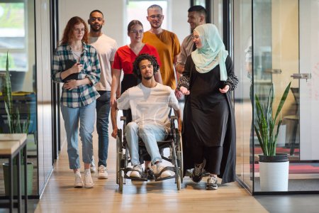 Un grupo diverso de jóvenes empresarios se congrega dentro de una moderna oficina cerrada en cristal de startups, con inclusión con una persona en silla de ruedas, un joven afroamericano y un hiyab.