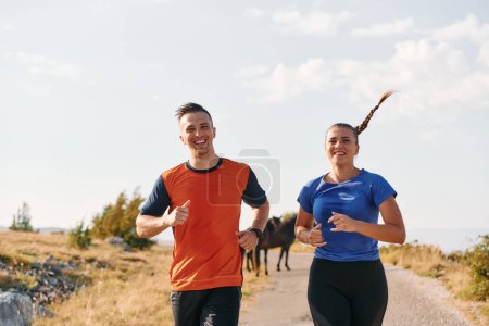 A couple dressed in sportswear runs along a scenic road during an early morning workout, enjoying the fresh air and maintaining a healthy lifestyle.