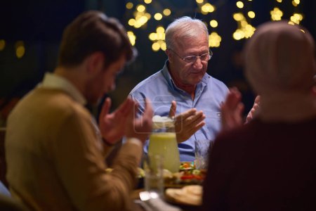 In einem modernen Restaurant-Ambiente trifft sich eine europäische islamische Familie während des Ramadan zum Iftar, um vor dem Essen zu beten und Tradition und zeitgenössische Gepflogenheiten in einer Feier zu vereinen.