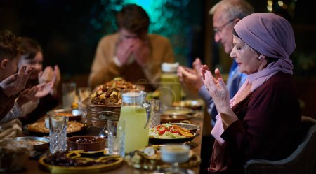 In einem modernen Restaurant-Ambiente trifft sich eine europäische islamische Familie während des Ramadan zum Iftar, um vor dem Essen zu beten und Tradition und zeitgenössische Gepflogenheiten in einer Feier zu vereinen.