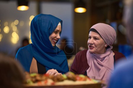 In a modern restaurant setting, a woman in hijab engages in conversation with her mother while they wait for the iftar meal, embodying familial bonding and cultural tradition during Ramadan