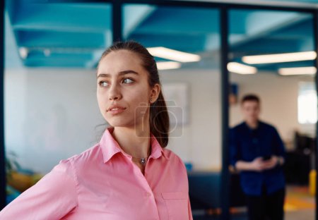 Portrait of young smiling business woman in creative open space coworking startup office. Successful businesswoman standing in office with copyspace. Coworkers working in background. 
