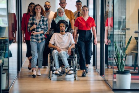 Un groupe diversifié de jeunes gens d'affaires se rassemble au sein d'un bureau vitré moderne de startups, mettant en vedette l'inclusion avec une personne en fauteuil roulant, un jeune homme afro-américain et un hijab