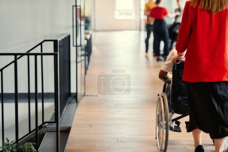 Une femme d'affaires aide son collègue en fauteuil roulant dans les couloirs élégants d'un bureau de démarrage moderne, incarnant l'inclusivité et le travail d'équipe. 