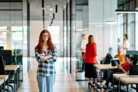 A portrait of a young businesswoman with modern orange hair captures her poised presence in a hallway of a contemporary startup coworking center, embodying individuality and professional confidence