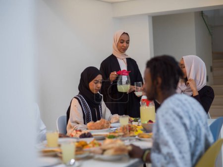 Eine vielfältige islamische Familie versammelt sich zum Iftar und feiert freudig ihr gemeinsames Fasten während des Ramadan, während eine muslimische Frau in einem wunderschönen Hijab anmutig Wasser zum Ende ihres Fastens gießt.