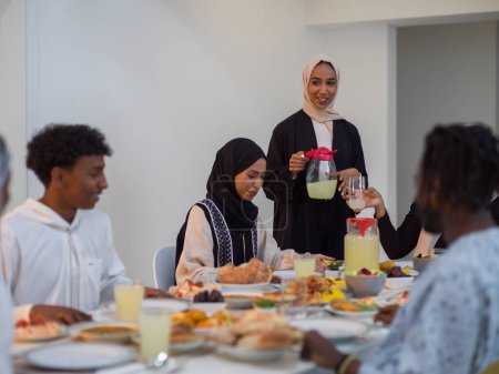 Una diversa familia islámica se reúne para iftar, rompiendo alegremente su ayuno durante el Ramadán, con una mujer musulmana en un hermoso hiyab que vierte agua con gracia para marcar el final de su ayuno