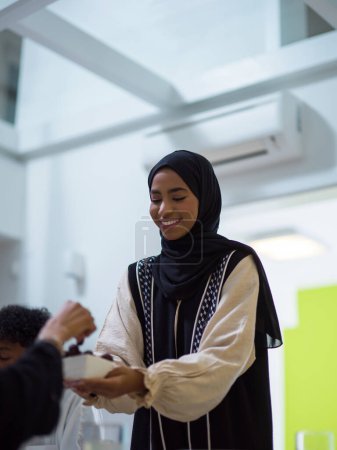 Una mujer en un hiyab extiende una bandeja de dátiles a su diversa familia, creando una escena de unidad y alegría mientras se reúnen para romper su ayuno durante el mes santo del Ramadán, simbolizando el
