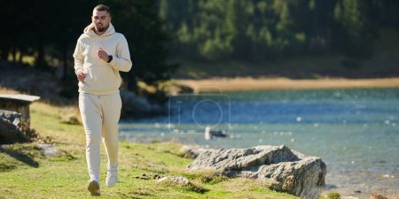  Der sportliche Mann bewahrt seinen gesunden Lebensstil, indem er durch die malerische Berg- und Seenlandschaft läuft, was ein Bekenntnis zu Fitness und Wohlbefinden zeigt. 