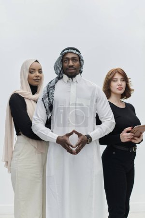 Téléchargez les photos : Homme d'affaires arabe se tient avec confiance aux côtés de deux femmes d'affaires, dépeignant une équipe déterminée et diversifiée qui incarne l'ambition, l'innovation et le leadership visionnaire sur un fond blanc immaculé - en image libre de droit