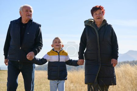 Elderly couple enjoys a leisurely stroll in nature with their grandchild, creating precious moments of intergenerational bonding amidst the serene and picturesque surroundings.