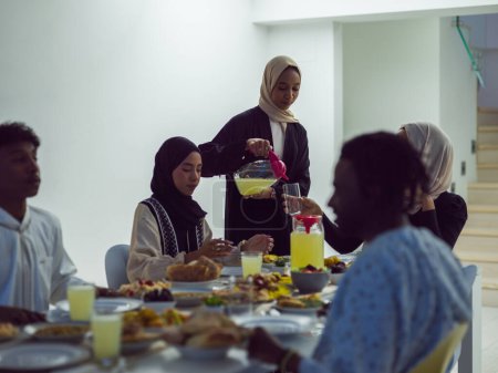 Une famille islamique diversifiée se rassemble pour iftar, rompant joyeusement leur jeûne pendant le Ramadan, avec une femme musulmane dans un magnifique hijab versant gracieusement de l'eau pour marquer la fin de leur jeûne