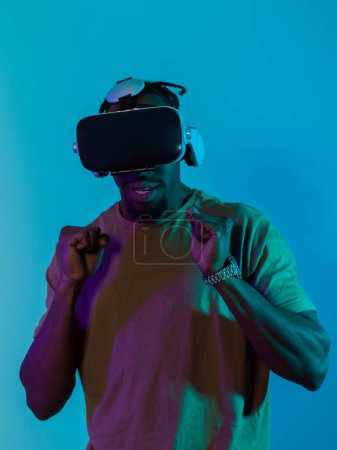 El hombre afroamericano se sumerge en una emocionante experiencia de juego de terror usando gafas VR, creando una atmósfera aislada e intensa sobre un llamativo fondo azul..