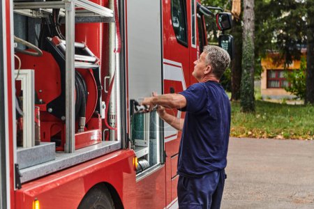 Un pompier dévoué prépare un camion de pompiers moderne en vue d'un déploiement dans des zones touchées par un incendie dangereux, démontrant ainsi son état de préparation et son engagement à intervenir en cas d'urgence. 