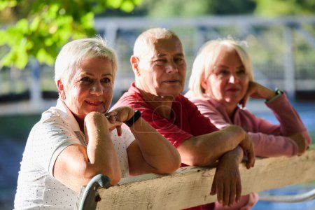 A group of elderly individuals, including a senior man and two older women, sits in a park on a sunny autumn day, embodying the concept of healthy aging through companionship, relaxation, and outdoor