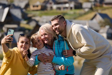 Strahlend vor Freude fängt eine glückliche Familie kostbare Momente in der Natur ein, während sie lächelt und lacht, während sie ein Selfie mit dem Smartphone macht und vor dem Hintergrund der