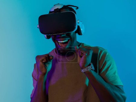 El hombre afroamericano se sumerge en una emocionante experiencia de juego de terror usando gafas VR, creando una atmósfera aislada e intensa sobre un llamativo fondo azul..