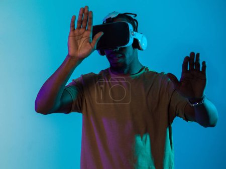 Foto de Inmerso en un reino digital, un hombre afroamericano navega por el paisaje virtual con gafas VR, utilizando gestos táctiles para interactuar con objetos virtuales, mostrando una mezcla armoniosa de - Imagen libre de derechos