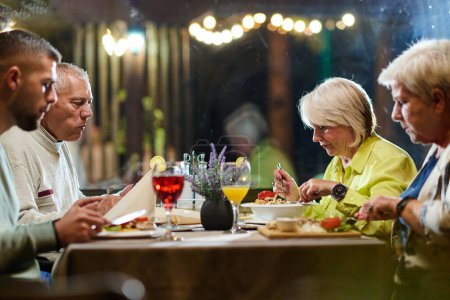 Foto de Un grupo de amigos de la familia, compuesto por un nieto joven y personas mayores, comparten una deliciosa cena en un restaurante moderno, ejemplificando el concepto de envejecimiento saludable a través de intergeneracionales - Imagen libre de derechos