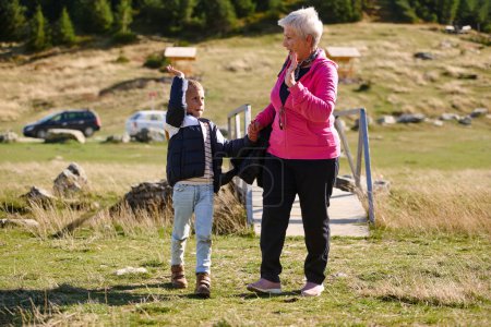 Die ältere Großmutter und ihr Enkelkind teilen sich einen gemütlichen Spaziergang durch die Natur, umhüllt von der Schönheit ihrer Umgebung, und fördern eine Bindung, die Generationen übergreifend ist.. 