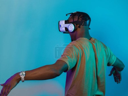 El hombre afroamericano se pone gafas VR, absorto en una simulación de realidad virtual, gesticulando con las manos, sobre un llamativo fondo azul, destacando la fusión de la tecnología de vanguardia y