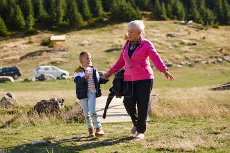 Die ältere Großmutter und ihr Enkelkind teilen sich einen gemütlichen Spaziergang durch die Natur, umhüllt von der Schönheit ihrer Umgebung, und fördern eine Bindung, die Generationen übergreifend ist.. 