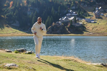  Der sportliche Mann bewahrt seinen gesunden Lebensstil, indem er durch die malerische Berg- und Seenlandschaft läuft, was ein Bekenntnis zu Fitness und Wohlbefinden zeigt. 