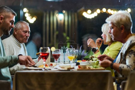 Un groupe d'amis de la famille, composé d'un jeune petit-fils et de personnes plus âgées, partagent un délicieux dîner dans un restaurant moderne, illustrant le concept de vieillissement en santé par le biais intergénérationnel