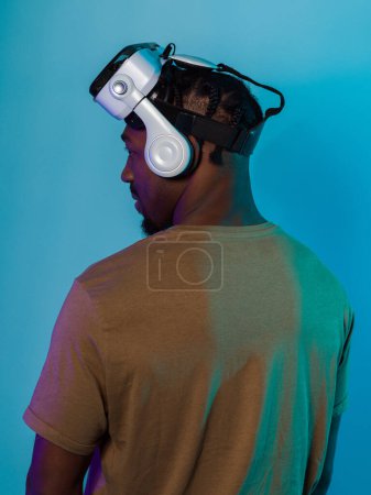En un visual futurista, un hombre afroamericano se encuentra aislado sobre un llamativo telón de fondo azul, adornado con gafas VR que lo transportan a una experiencia de realidad virtual de vanguardia, fusionándose