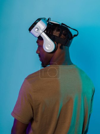 In einem futuristischen Visual steht ein afroamerikanischer Mann isoliert vor einem auffallend blauen Hintergrund, geschmückt mit einer VR-Brille, die ihn in eine hochmoderne Virtual-Reality-Erfahrung versetzt.