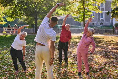 Eine Gruppe von Senioren folgt einem Trainer, der im Park Outdoor-Übungen durchführt, während sie gemeinsam danach streben, Vitalität und Wohlbefinden aufrechtzuerhalten, indem sie einen aktiven und gesundheitsbewussten Lebensstil pflegen.