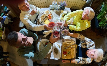 Top view photo of a modern multi generational family, including grandparents and a grandchild, raises a toast during a joyful dinner, epitomizing the warmth and unity shared across generations in