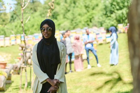 Afroamerikanisch-muslimische Frau im Hijab erkundet natürliche Bienenfarmen für die Honigproduktion und verbindet Tradition mit Nachhaltigkeit in der ruhigen Landschaft. 