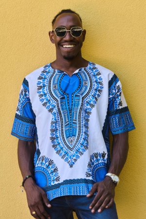 A vibrant portrait of an African American teenager proudly wearing traditional Sudanese clothing against a striking yellow background. 