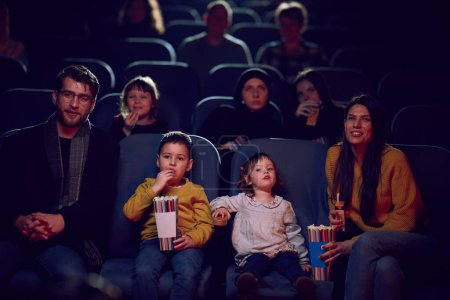 Eine moderne Familie genießt die gemeinsame Zeit im Kino und gönnt sich Popcorn, während sie mit ihren Kindern einen Film schaut.