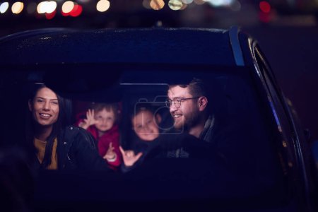 Dans les heures nocturnes, une famille heureuse profite de moments ludiques ensemble à l'intérieur d'une voiture alors qu'ils voyagent sur une route nocturne, éclairés par la lueur des phares et remplis de rire et de joie.
