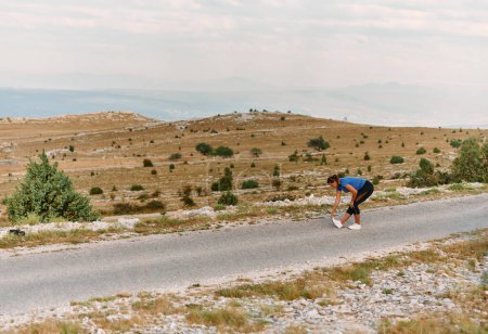 Una atleta decidida estira sus músculos después de una extenuante carrera a través de escarpados terrenos montañosos, rodeada de impresionantes paisajes rocosos. 