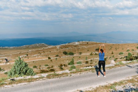 Una atleta decidida estira sus músculos después de una extenuante carrera a través de escarpados terrenos montañosos, rodeada de impresionantes paisajes rocosos. 