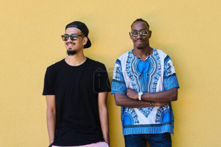 Eine Darstellung der Kameradschaft und kulturellen Vielfalt zweier männlicher Freunde, einer davon ein afroamerikanischer Teenager in traditioneller sudanesischer Kleidung, angelehnt an eine leuchtend gelbe Wand