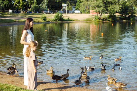 Téléchargez les photos : Mom and daughter feeding ducks in a park on the lake. Summer time. - en image libre de droit