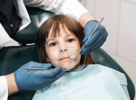 Foto de People, medicine, stomatology, technology and health care concept. Professional young male dentist working with little girl in clinic. - Imagen libre de derechos
