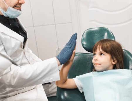 Foto de Family dentist and little girl give each other five. Doctor and child Scratch the palms. Dental modern clinic. Pediatric shake hands with child girl. - Imagen libre de derechos