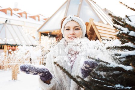 Photo for Charming young woman in winter clothes plays with snowflakes next to the Christmas tree, winter, christmas market. - Royalty Free Image