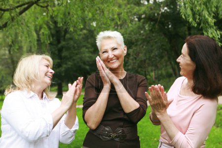 Glückliche Rentnerinnen treffen sich im Park. Drei Freundinnen im Park feiern Geburtstag. Klatscht in die Hände, gratuliert, jubelt. Das Konzept von älteren Menschen, Freundschaft und Emotionen.